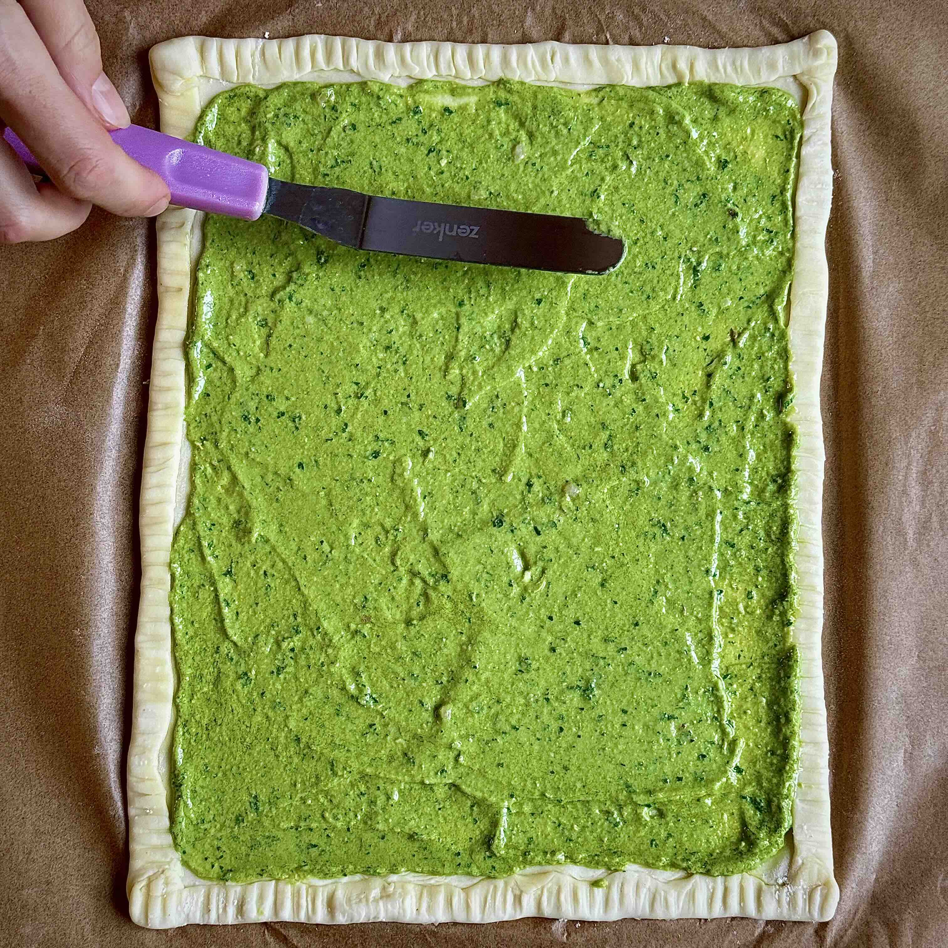 Puff pastry with a smooth layer of green pesto spread across