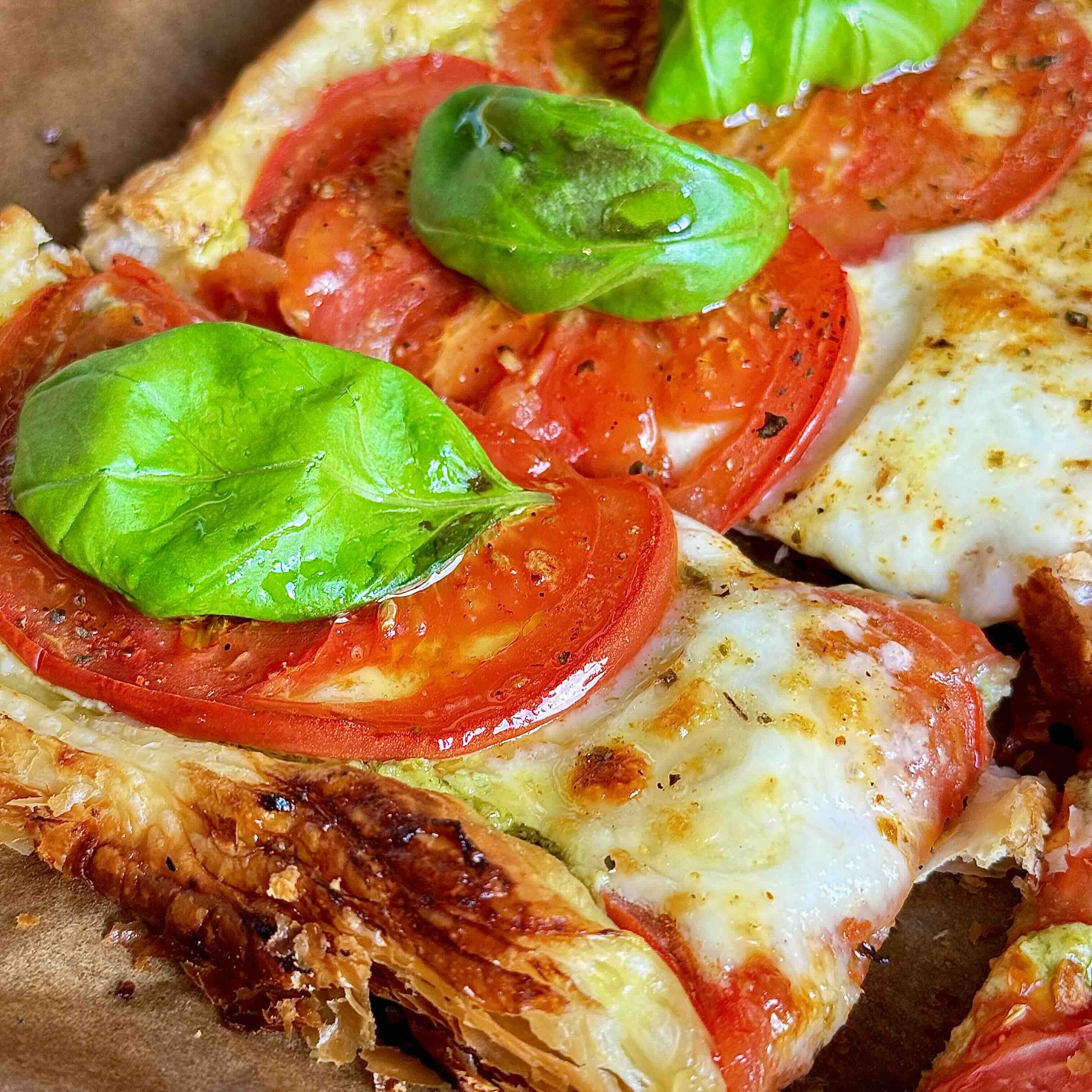 Finished puff pastry pizza garnished with bright green basil leaves.